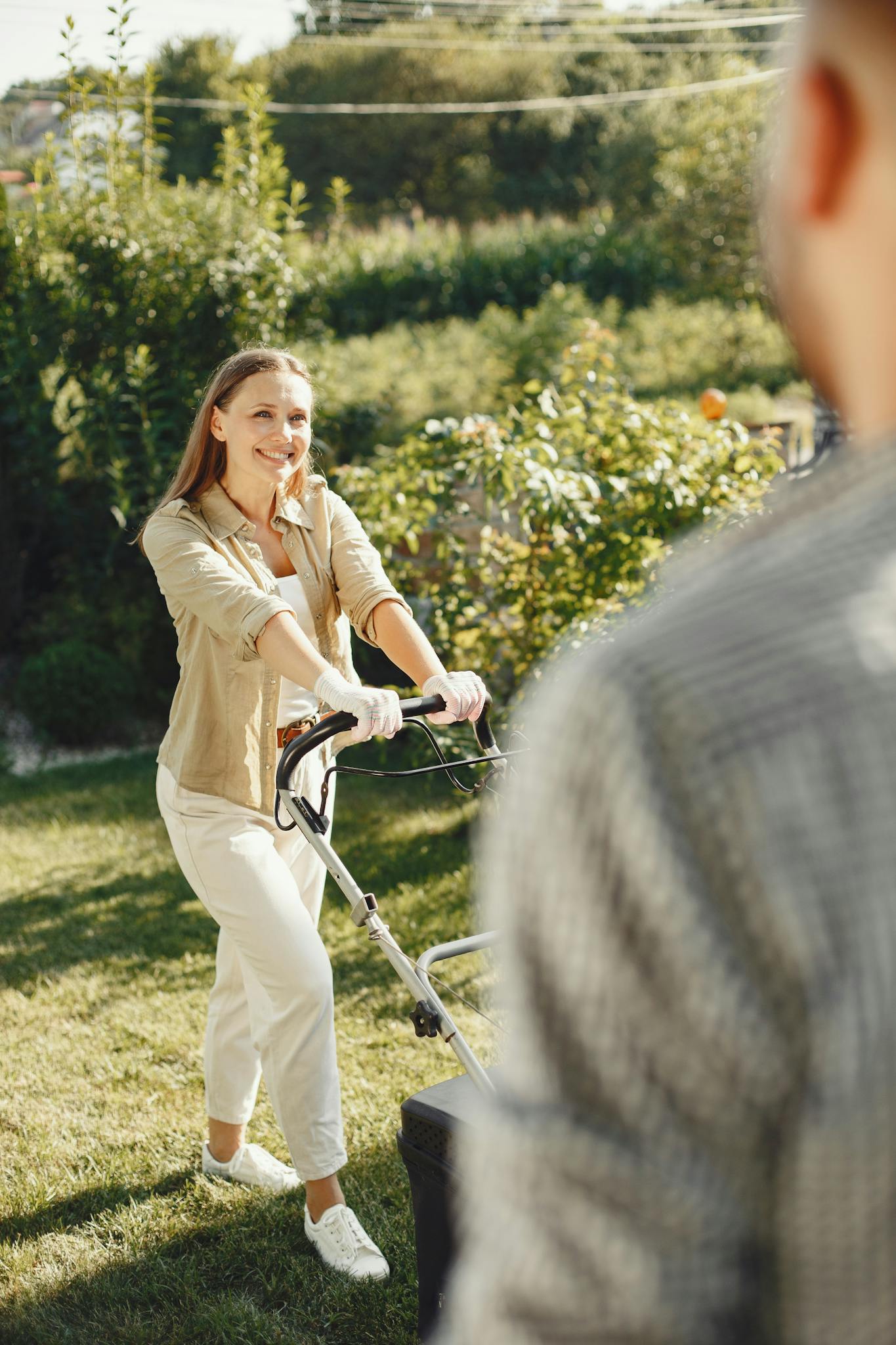 Smiling woman mowing the lawn in a sunny backyard garden.